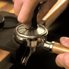 Espressomehl wird mit einem Tamper in den Siebträger gepresst